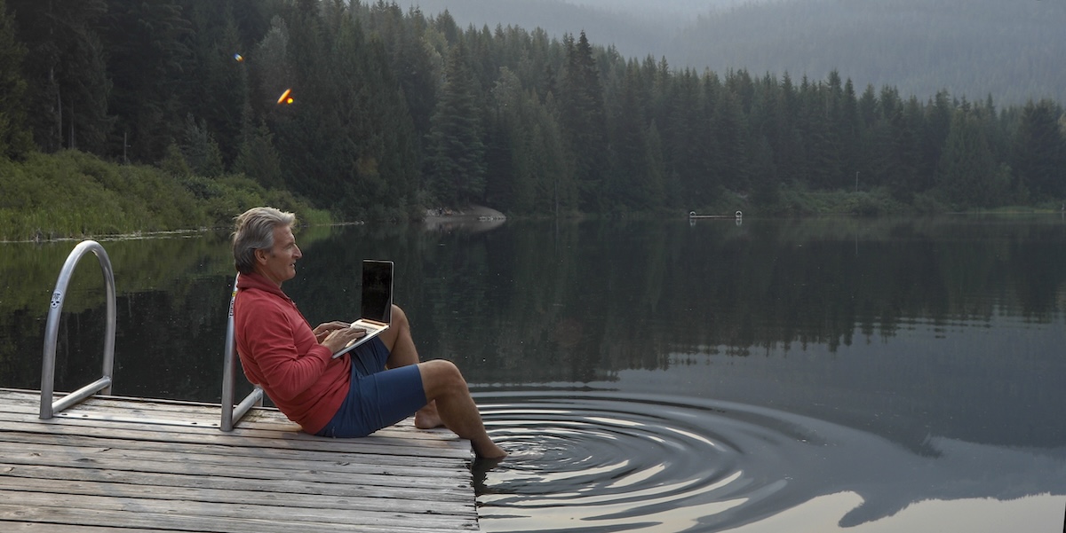 Mann mit Laptop an Badesee